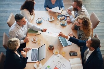 Diverse group in a meeting, discussing business. Teamwork around a table, with laptops and documents. Collaborative business meeting, diverse professionals. Business people working over lunch at cafe.