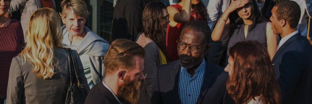 A diverse group of professionals, including men and women of various ethnicities, engage in conversation and networking. Business people bustling social event. Business community vibes - Powered by Adobe