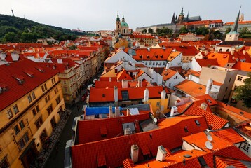 Aerial view of Prague Old Town, capital of Czech Republic & a UNESCO heritage city, with the castle on a hilltop, St. Nicholas Church in Lesser Town & red rooftops of historical houses by a street 