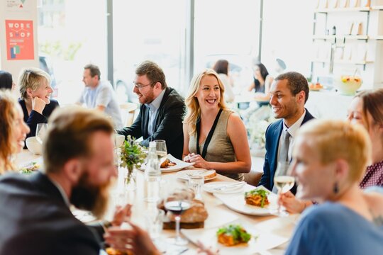 A diverse group of people enjoying a lively dinner party. The scene features men and women of various ethnicities, sharing laughter and delicious food at a beautifully set table.