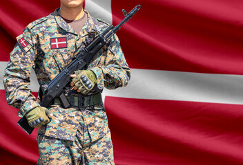 Fototapeta premium Denmark flag with soldier in military uniform holding assault rifle in front of it