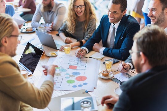 Diverse group in a business meeting, discussing plans. Laptops and documents on the table. Smiling professionals collaborating in a modern office setting. Business people in a creative meeting. - Powered by Adobe