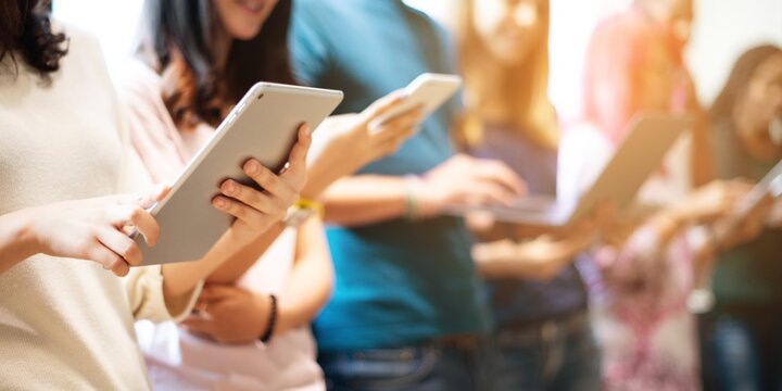 Diverse group of people using tablets, standing in a line. Casual setting, diverse group, technology in use. Tablets in hands, digital devices and technology concept, background with copy space.