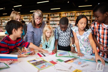 Diverse group of children and a teacher in a library, exploring maps and books. Engaged students, multicultural learning, educational environment, teamwork. Elementary school kids learning in class.