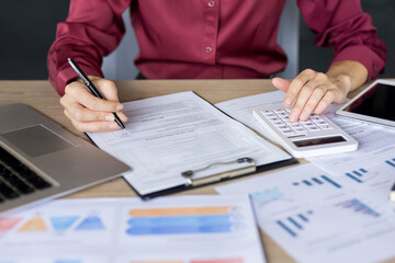 Accountant hands calculating finances and reviewing documents at a cluttered desk with laptop,...