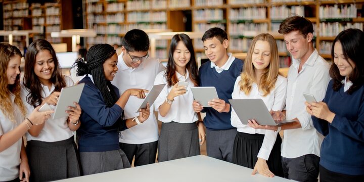 Diverse group of students in a library using tablets. Students engaged with technology. Diverse students learning with tablets in library. Diverse young men and women students using tablet in library - Powered by Adobe
