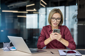 Young businesswoman with glasses receiving upsetting news on her mobile phone, expressing worry and...