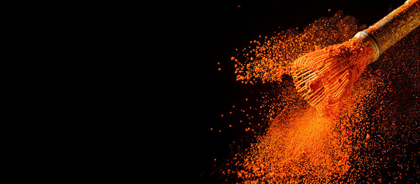 Vibrant orange powder exploding from makeup brush on dark background  cosmetic concept