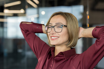 Smiling young businesswoman wearing glasses and a red blouse relaxing at the modern office with...