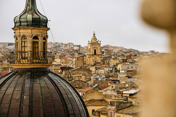 Panoramic View Over Ragusa From Cathedral Of San Giovanni Battista: Historic Sicilian City Rooftops, Church Domes, And Dense Stone Architecture Under Overcast Sky