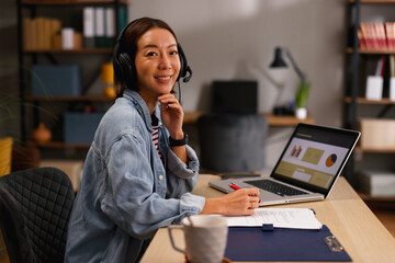 Smiling asian woman joining a virtual call from her comfortable home office