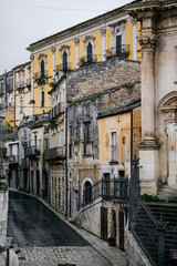 Historic Urban Architecture In Ragusa, Sicily: Weathered Stone Buildings, Narrow Streets, Layered Rooftops, And Church Dome Forming Dense Mediterranean Cityscape