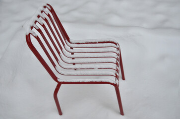 Closeup snow covered red metal chair standing on snow background.