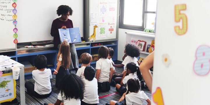 A teacher reads to a diverse group of young students in a classroom. Diverse children sit attentively, listening to the teacher. Classroom and learning. Education and knowledge concept.