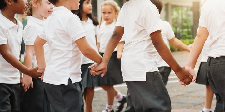 Group of diverse children holding hands in a circle outdoors. Children in school uniforms, playing and smiling. Happy students enjoying playtime together in a outdoor school. Diverse students