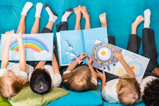 Children reading colorful books on a blue couch. Kids enjoy stories, books, and reading. Diverse group of children, books, and colorful pages. Little kids reading books together.