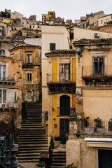 Historic Urban Architecture In Ragusa, Sicily: Weathered Stone Buildings, Narrow Streets, Layered Rooftops, And Church Dome Forming Dense Mediterranean Cityscape