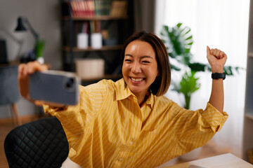 Asian woman smiling and raising fist during a video call on a smartphone