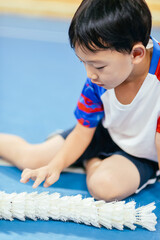 Seven-year-old Asian boy sitting on an indoor court floor and organizing shuttlecocks