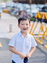 Happy seven-year-old Asian boy in white shirt walking and laughing on the street after school