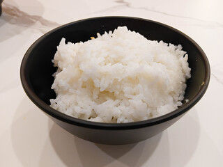 Steamed jasmine rice served in a black bowl on a clean white table, simple Asian food concept, fresh cooked rice for daily meals.