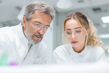 Fototapeta premium A focused discussion between two scientists in lab coats, analyzing data or samples in a modern laboratory setting.
