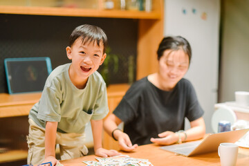 Asian mother and seven-year-old son playing card games together in a cozy home indoor setting