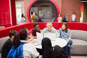 Diverse group of students studying together, using laptops. Collaborative learning in a modern space. Engaged students, teamwork, technology in education. Students working on laptop in school.