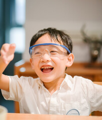 Happy seven-year-old Asian boy wearing blue safety goggles and laughing during a home science experiment