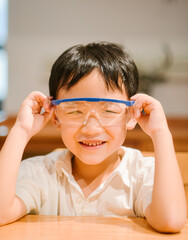 Happy seven-year-old Asian boy wearing blue safety goggles and laughing during a home science experiment