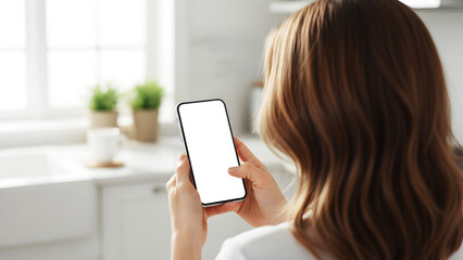 Hand holding mobile smartphone with blank white screen mockup in modern bright kitchen interior background, woman using device for smart home automation and digital lifestyle app design.
