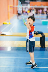 Seven-year-old Asian boy practicing badminton with a racket in an indoor sports gymnasium