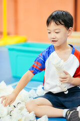 Seven-year-old Asian boy sitting on an indoor court floor and organizing shuttlecocks