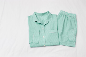 Top view of folded mint green striped pajama set on white bed. Minimal style, cozy, comfort...