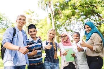 Obraz premium Diverse group of happy young adults smiling in a park. Multicultural friends, including young men and young women. Diverse young people enjoying time together outdoors.