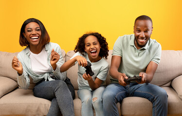 Domestic entertainment. Emotional black dad and daughter holding joysticks, competing with each...