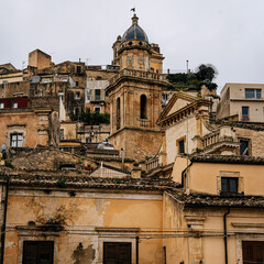 Historic Urban Architecture In Ragusa, Sicily: Weathered Stone Buildings, Narrow Streets, Layered Rooftops, And Church Dome Forming Dense Mediterranean Cityscape