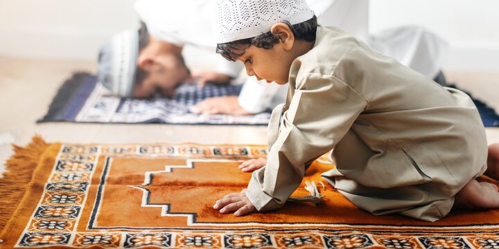 A young Arab boy in traditional attire prays on a prayer mat, showcasing devotion. The boy's focus on prayer highlights the importance of faith in daily life.