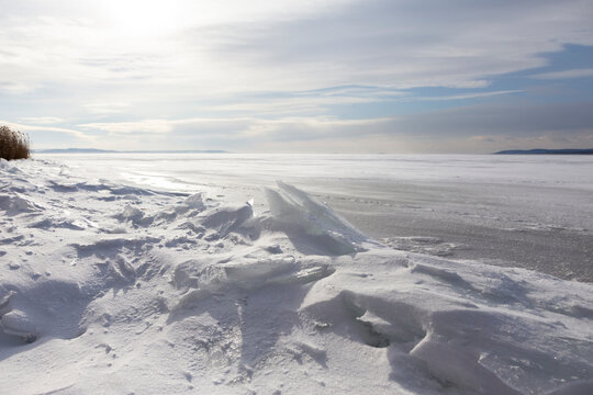 Schneeverwehungen am gefrorenen See unter winterlichem Himmel