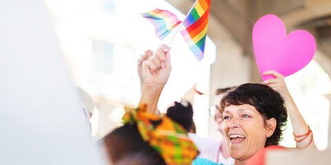 A person at a pride parade holding a rainbow flag and a pink heart. The pride parade is vibrant...