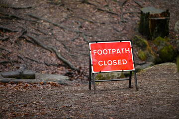 A red Footpath closed sign on a leafy walkway in the forest. 