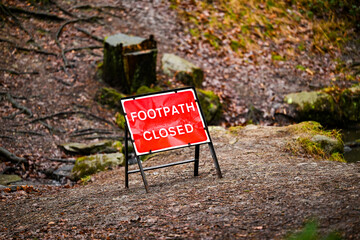 A red Footpath closed sign on a leafy walkway in the forest. 