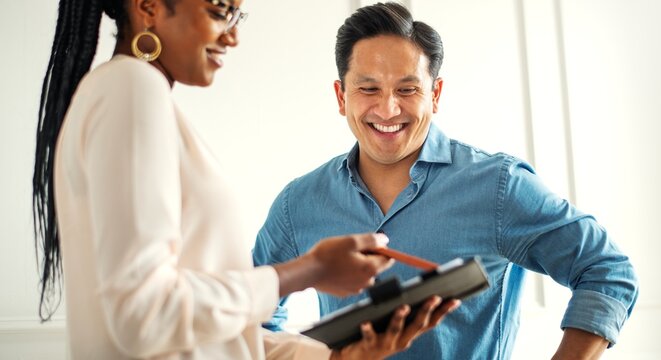 A smiling man and woman discussing work. The man, in a blue shirt, and the woman, in glasses, collaborate on a project. Productive work discussion. Hispanic businessman with colleauge in office.
