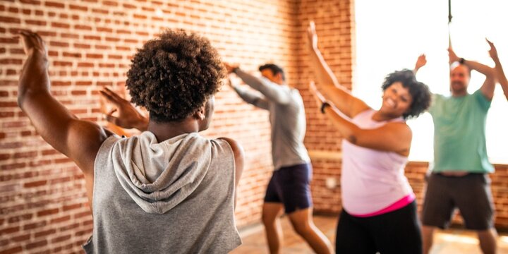 Group dance class with diverse participants in a bright studio. People enjoying dance, following the instructor. Energetic dance session in a lively atmosphere. Diverse people in gym class.