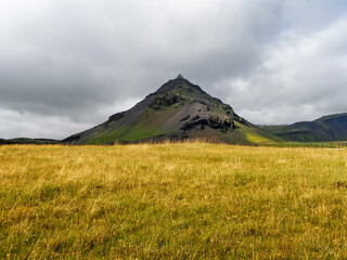 Wild Icelandic landscape with visible Stapafell volcanic mountain, against dark cloudy sky. This palagonitic pyramide is 526 m in height. Hellnar, Arnarstapi, Sn&aelig;fellsnes Peninsula in western Iceland.
