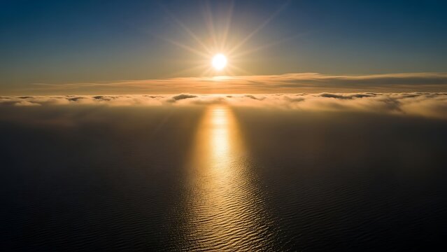 Aerial view of golden sunrise or sunset over the ocean with sun rays reflecting on water and fog layer below - Powered by Adobe