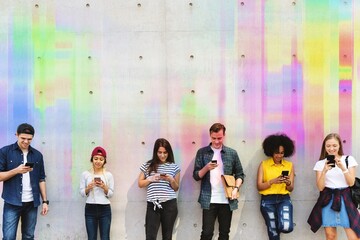 Naklejka premium Group of young adults outdoors using smartphones together and chilling