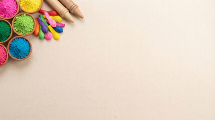 Vibrant holi color powders in bowls on beige background with crayons and colorful sticks for festive celebration