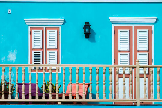 View of a vibrant turquoise facade adorned with white-trimmed windows and a wooden balcony, capturing the essence of Caribbean charm, Willemstad, Curacao.