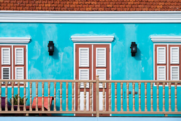 View of a vibrant turquoise facade adorned with white-trimmed windows and a terracotta roof, captured from a ground perspective, Willemstad, Curacao.